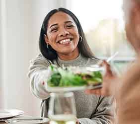 Smiling woman passing salad at table