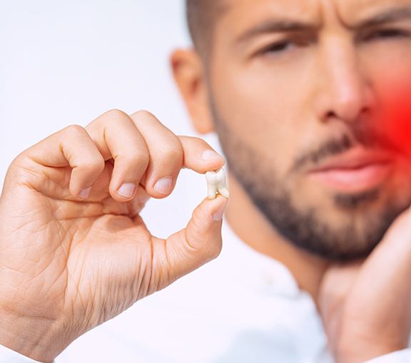 Man holding one hand to inflamed jaw while holding up extracted tooth