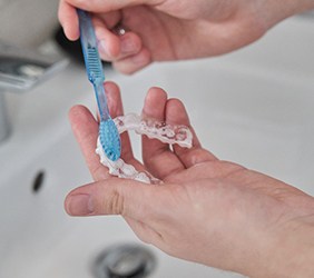 Patient using toothbrush to clean aligner