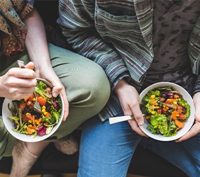 Bird’s eye view of two people in casual clothes holding salad bowls in their laps