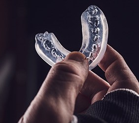 Fingers holding up a clear mouthguard with a dark background