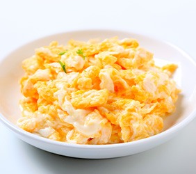 Scrambled eggs with a bit of chive in a white bowl with white background