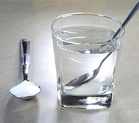 Glass of water with a spoon next to a spoon full of salt on a gray counter