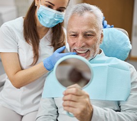 Man with white hair looking at reflection in dental chair next to dentist