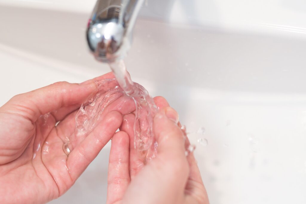 Patient rinsing clear aligner in sink with water